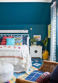 a bedroom with teal walls and white bedding, colorful pillows and rugs