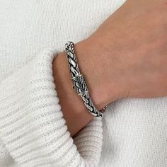 a person wearing a white sweater with a black and silver braid bracelet on their wrist