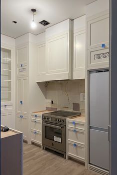 an empty kitchen with white cabinets and silver stove top oven, surrounded by blue tape on the walls