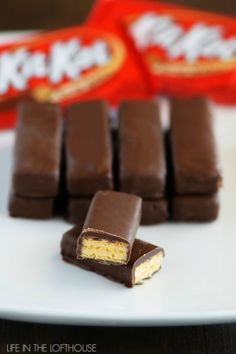 several pieces of chocolate on a white plate with candy in the background and two bags of crackers behind them