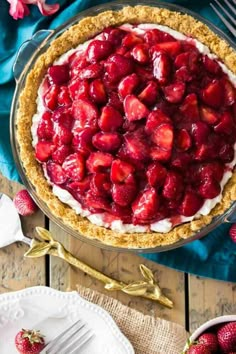 a pie topped with strawberries on top of a wooden table next to plates and forks