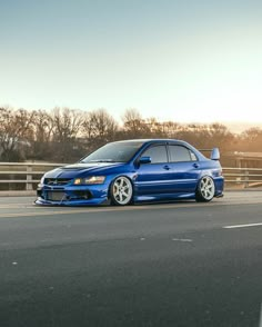 the blue car is parked on the side of the road in front of a fence