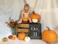 a baby sitting on top of a crate with pumpkins