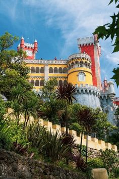 a large castle sitting on top of a lush green hillside next to trees and bushes