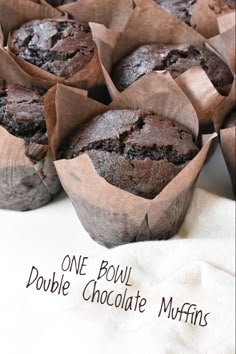 chocolate muffins in paper cups on a white cloth with the words bakery style double chocolate muffins