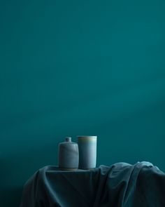 two vases sitting on top of a table covered in a black cloth next to a green wall