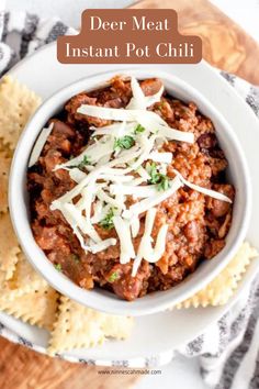 a white bowl filled with beef and cheese next to crackers on a wooden table