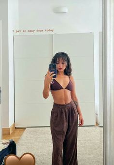 a woman taking a selfie in front of a mirror with her cell phone and wearing brown pants