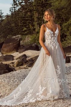 a woman in a white wedding dress standing on rocks near the ocean with trees behind her