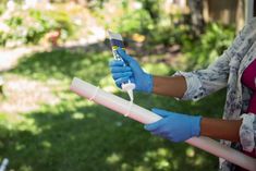 a woman in blue gloves is holding a toothbrush and an object that looks like a tube of toothpaste