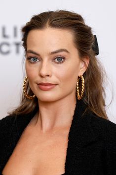 a woman with large gold hoop earrings on her head and wearing a black jacket, posing for the camera