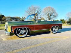 a green and brown truck parked in a parking lot next to another car with chrome rims