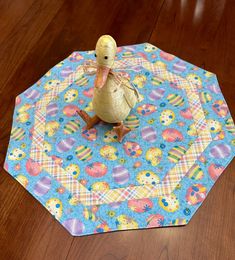 a toy duck sitting on top of a blue and yellow table cloth covered in flowers