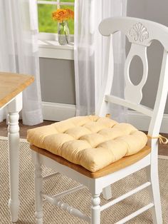 a white chair with a cushion on it in front of a table and windowsill