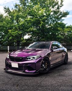 a purple bmw car parked in a parking lot next to some trees and bushes on a sunny day