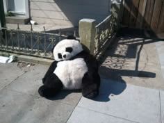 a stuffed panda bear sitting on the sidewalk in front of a fence and gated area