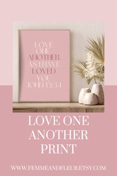 a pink poster with the words love one another print on it and a plant next to it