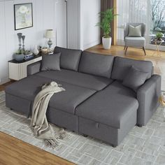 a large gray couch sitting in a living room on top of a wooden floor next to a window