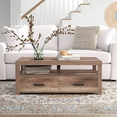 a living room with a white couch, coffee table and stair case in the background