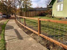 a wooden and wire fence next to a sidewalk in front of a green house on a sunny day