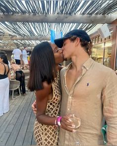 a man and woman kissing each other while standing on a wooden deck with people in the background