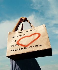 a woman carrying a bag with the words spirit of new generation painted on it in front of a blue sky