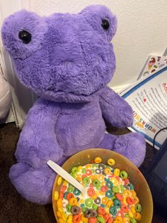 a purple teddy bear sitting next to a bowl of cereal