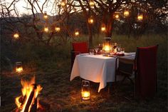 a dinner table with candles lit in front of an open fire pit