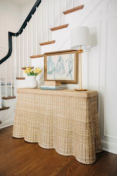 a table with a painting on it next to a stair case and flowers in a vase