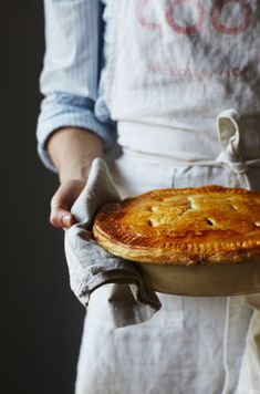 a person in an apron holding a pie