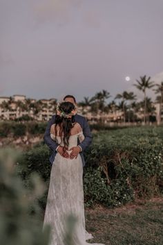 a bride and groom standing in front of the ocean at sunset with their arms around each other