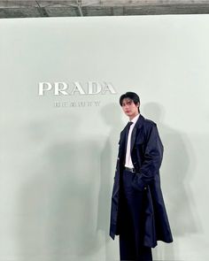 a man standing in front of a prada sign wearing a long coat and tie