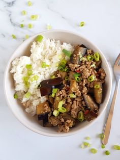 a white bowl filled with rice and meat on top of a table next to a spoon