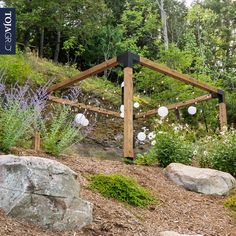 a wooden structure sitting on top of a hill next to rocks and flowers in front of trees