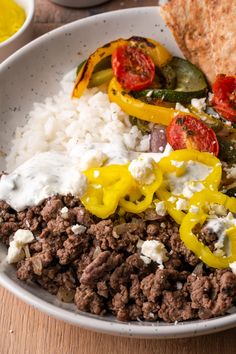 a white plate topped with meat and veggies on top of rice next to bread