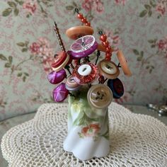 a vase filled with lots of different types of buttons on top of a doily