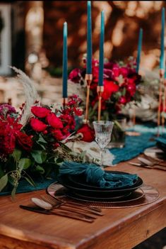 the table is set with red flowers and blue napkins, silverware, and candles