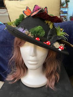 a white mannequin head wearing a black hat with flowers and butterflies on it