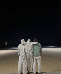 two men standing on the beach at night with their backs to each other, facing the ocean