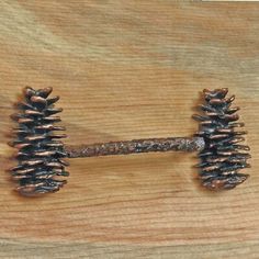 two pine cones are attached to a metal hook on a wooden surface with nails sticking out of it