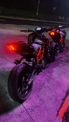 two motorcycles parked next to each other in the street at night time with bright lights on them