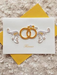 two gold wedding rings on top of a white card next to a yellow envelope with the word forever