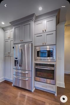 a stainless steel refrigerator and oven in a kitchen with white cabinets, wood floors and hard wood flooring