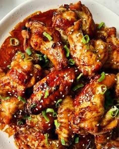 a white plate topped with chicken wings covered in sauce and sesame seeds, garnished with green onions