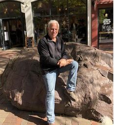 a man sitting on top of a large rock in front of a storefront window