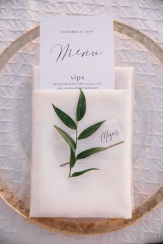 a place setting with napkins and greenery on it, along with a menu