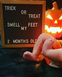 a baby laying next to a sign that says trick or treat smell my feet 2 months old