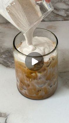 someone pouring something into a glass on top of a marble countertop in preparation to make an ice cream sundae