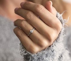 a woman's hand with a diamond ring on her left wrist, wearing a gray sweater