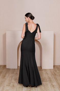 the back of a woman in a black dress standing on a wooden floor with her hands behind her back